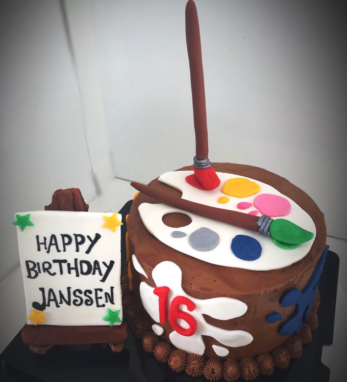 Chocolate cake with rich chocolate buttercream, decorated with a handcrafted birthday card, painter palette and brushes