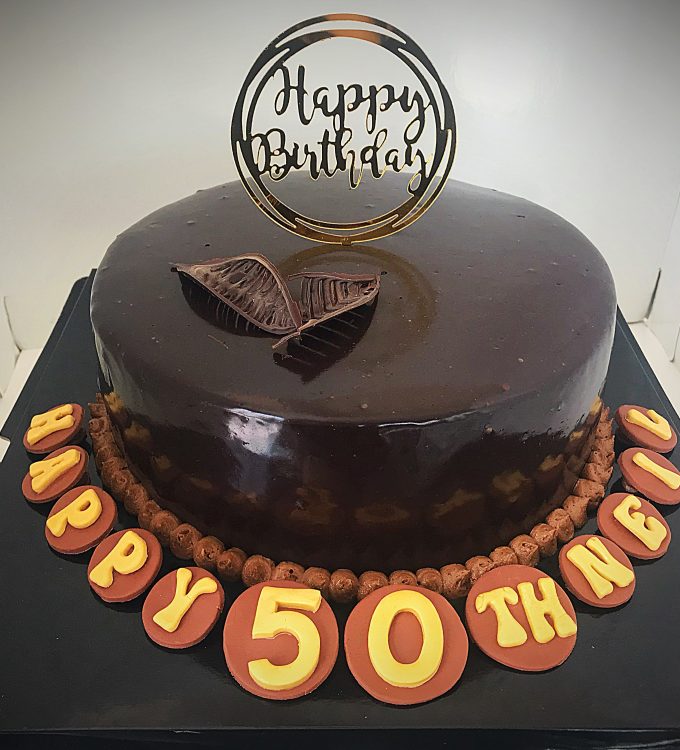 Chocolate cake with chocolate buttercream frosting and chocolate mirror glaze, tempered chocolate leaves and handcrafted 50th birthday message